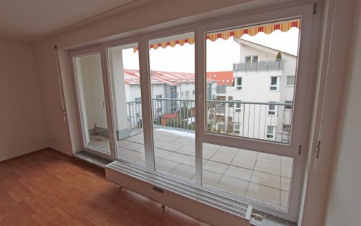 Blick durch Fensterfront auf dahinterliegenden Balkon mit Markise