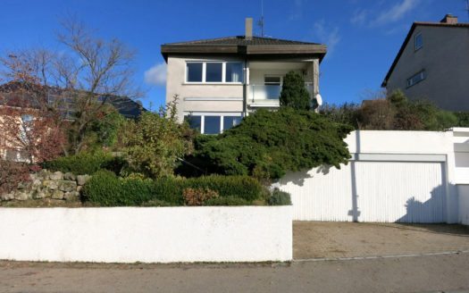 Frontansicht eines Einfamilienhauses mit zwei Garagen und weißer Mauer