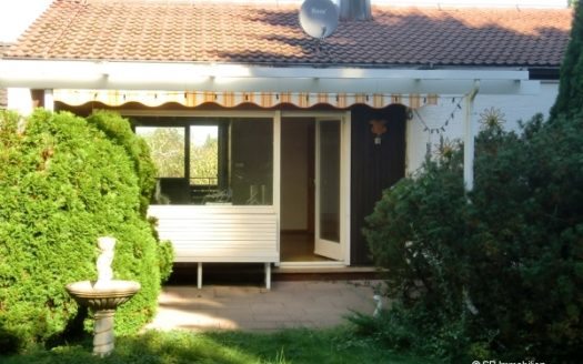 Bungalow mit Steinbrunnen, Hecke und weiß gestrichener Terrassentüre