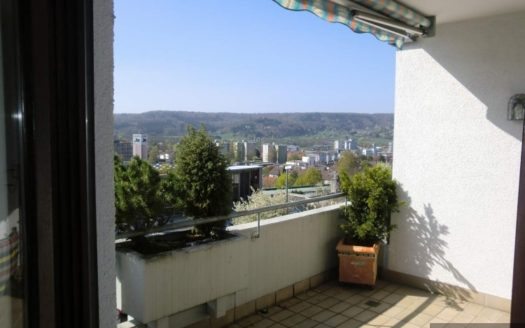 Braun gefliester Balkon mit bunter Markise und kleinem Buxbaum