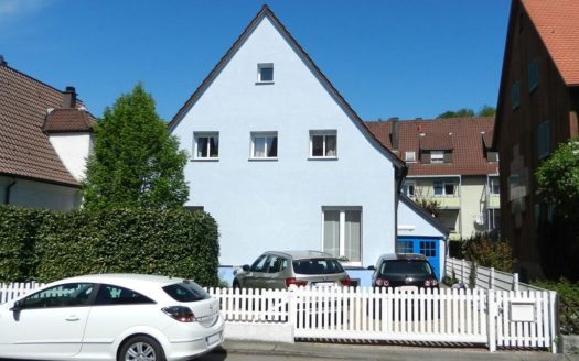 Forntansicht eines hellblauen Einfamilienhauses mit kleinen Fenstern