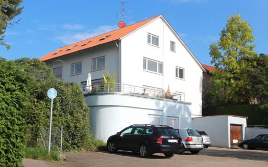 Weißes Mehrparteienhaus mit parkenden Autos und Dachgarten