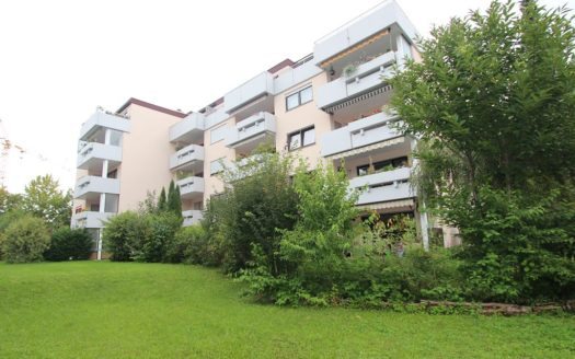 Großer Vorgarten mit Bäumen und Sträuchern, dahinter Wohnhaus mit weißen Balkonen