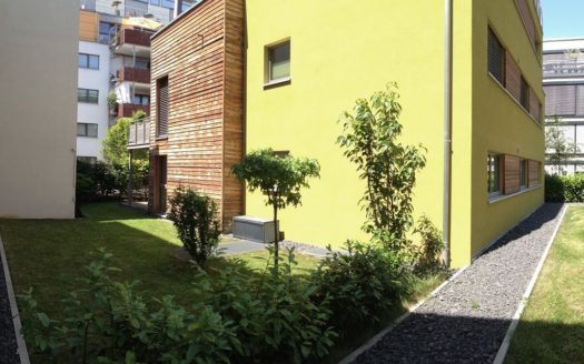 Gelb gestrichenes Haus mit Holzeinsätzen an den Fenstern und schwarzem Kiesweg