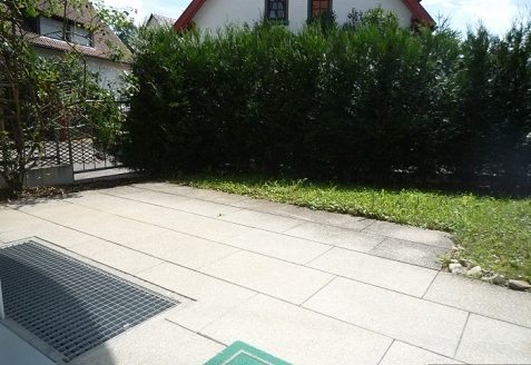 Steinterrasse mit kleinem Rasenstück und Heckenbüsche