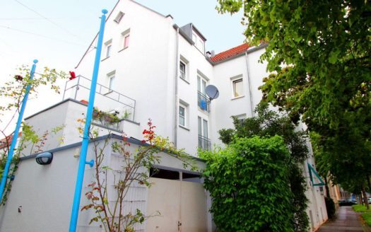 Gepflasterter Weg vor Wohngebäude mit Hecke und Satellitenschüssel