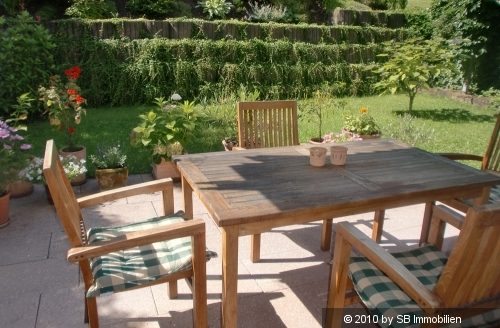 Teakholz Möbel auf Terrasse mit Steinfliesen, dahinter schön angelegter Garten