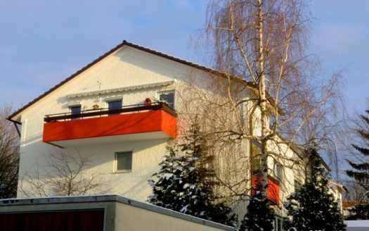 Frontansicht eines weißen Einfamilienhauses mit orangem Balkon