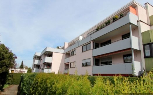 Rückseite eines Wohnhauses mit Hecke und grauen Balkonen
