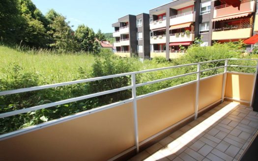 Hellbraun gefliester Balkon mit ockerfarbener Brüstung und Blick auf hohes Gras
